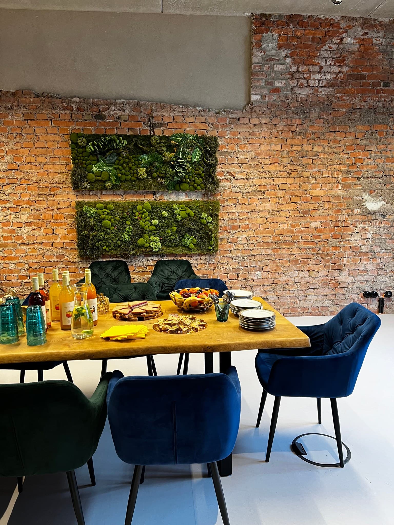 Zwei Moosbilder an der Backsteinwand von Werkraum.02, davor der gedeckte Konferenztisch mit Säften, Obst und Tellern zwischen blauen und grünen Samtstühlen