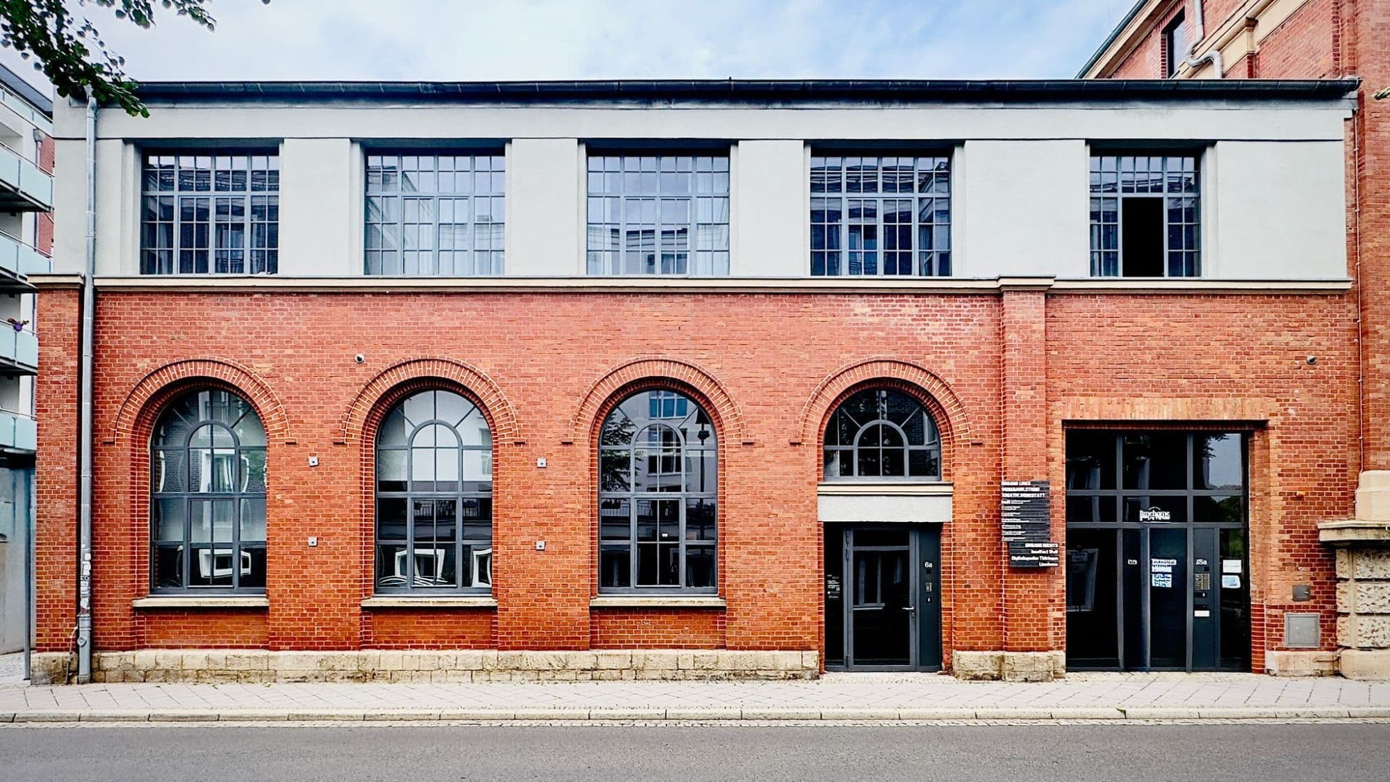Das Haus des Studios von vorn: im Erdgeschoss aus Backstein vier Rundbögen, unter dem vierten die Eingangstür mit der Nummer 6a, rechts ein verglastes Tor, im grau verputzten Obergeschoss fünf Sprossenfenster